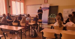 w ławkach siedzą dzieci, przed nimi  znajduję się policjantka