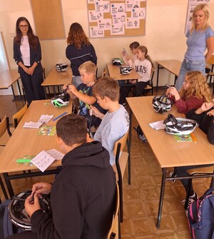 dzieci siedzą w ławkach  i ogadają otrzymane  kaski