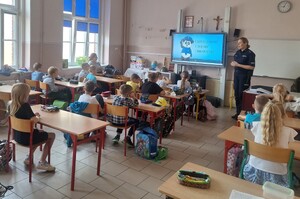policjanta stoi w sali, a dzieci  siedzą w ławkach